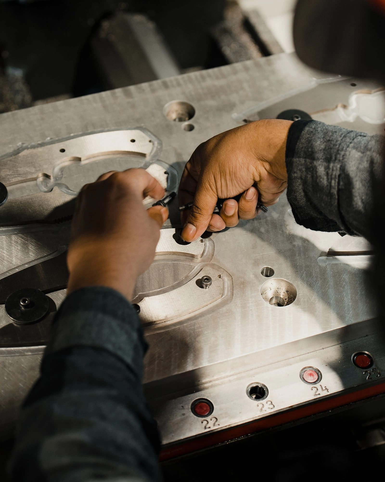 Hands setting screws into a machined fixture plate