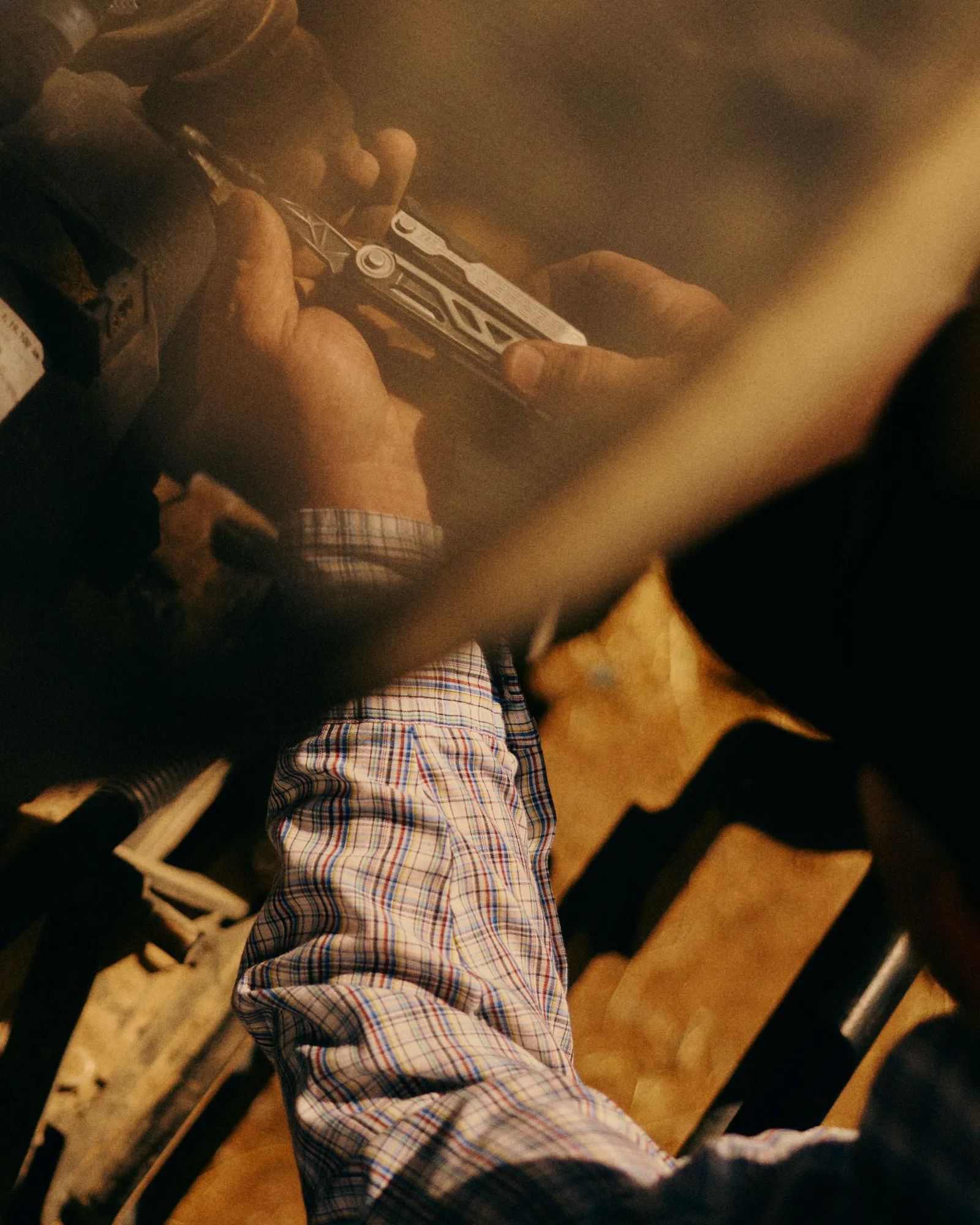 Hands working a multitool over a workbench, in warm light