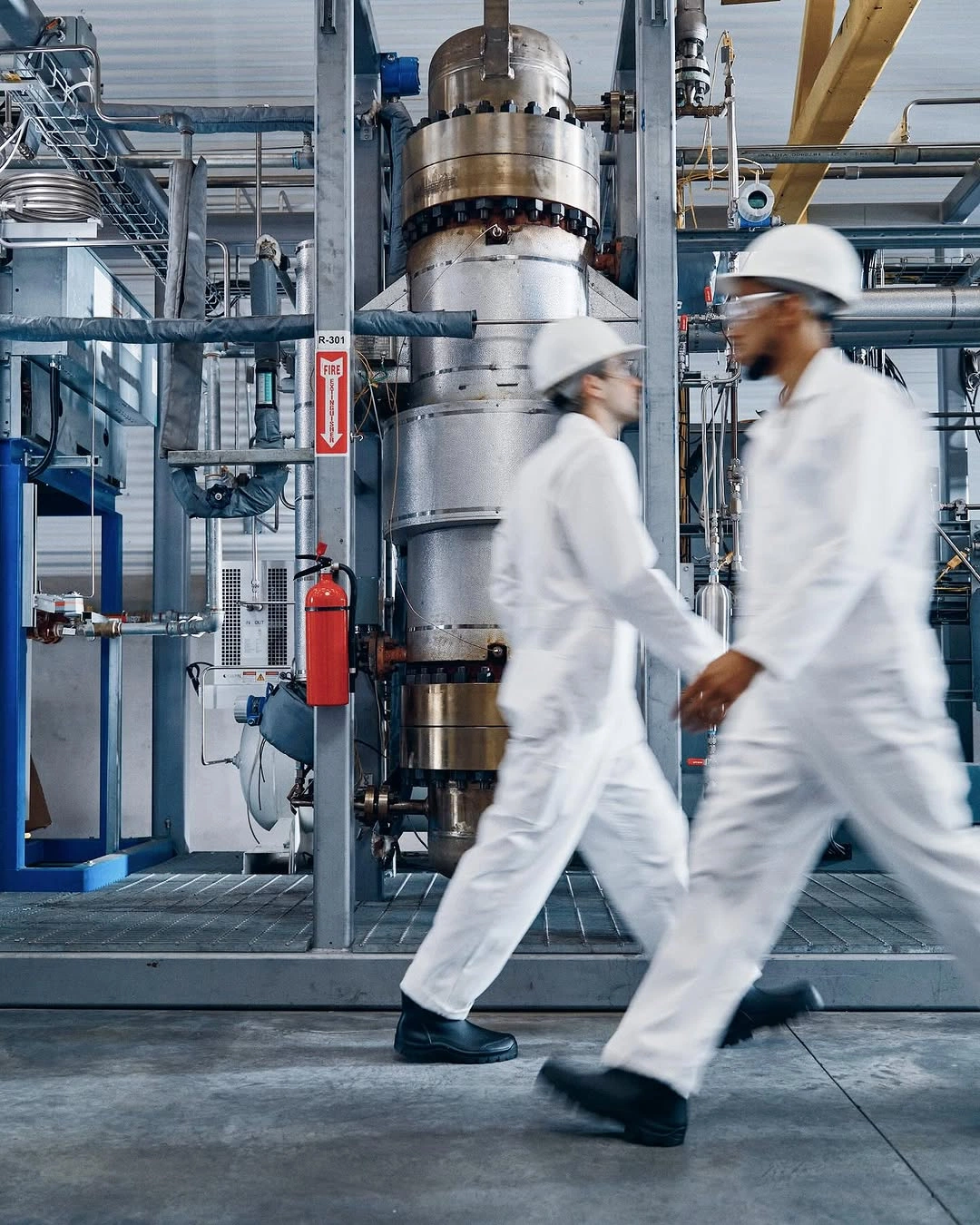 Two people in white coveralls and hard hats walking through a plant