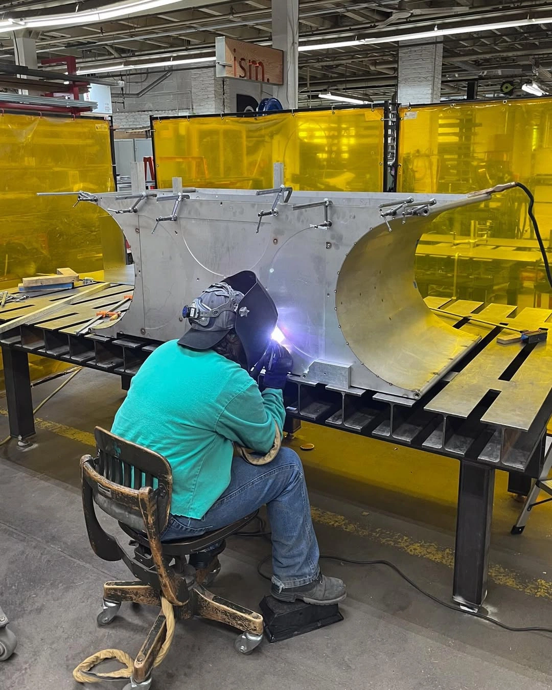 A welder at an aluminum assembly behind yellow welding curtains